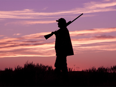 Ein Silhouette eines Jägers mit Gewehr vor einem bunten Sonnenuntergang.